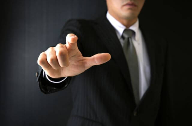 こちらを指さすスーツの男性
